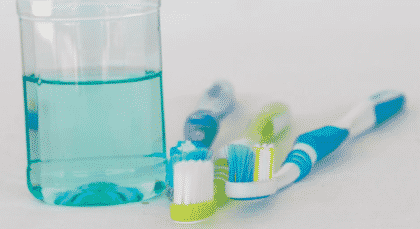 white counter with glass of turquoise mouthwash and three toothbrushes